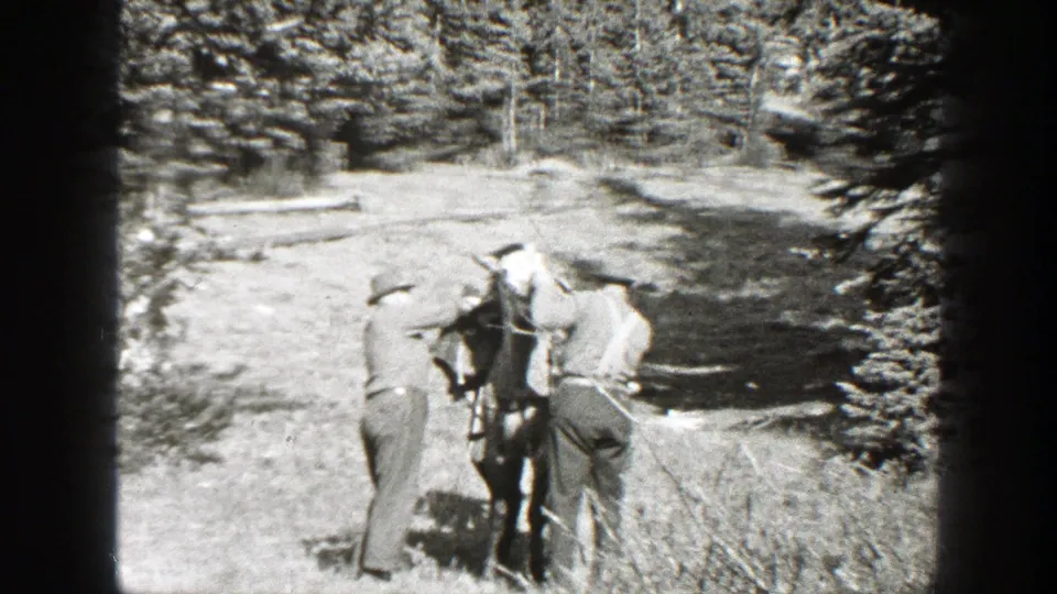 Two men adjust the horse's equipment from opposite sides in a sunlit forest clearing, consistent with the 1938 California home-movie metadata.