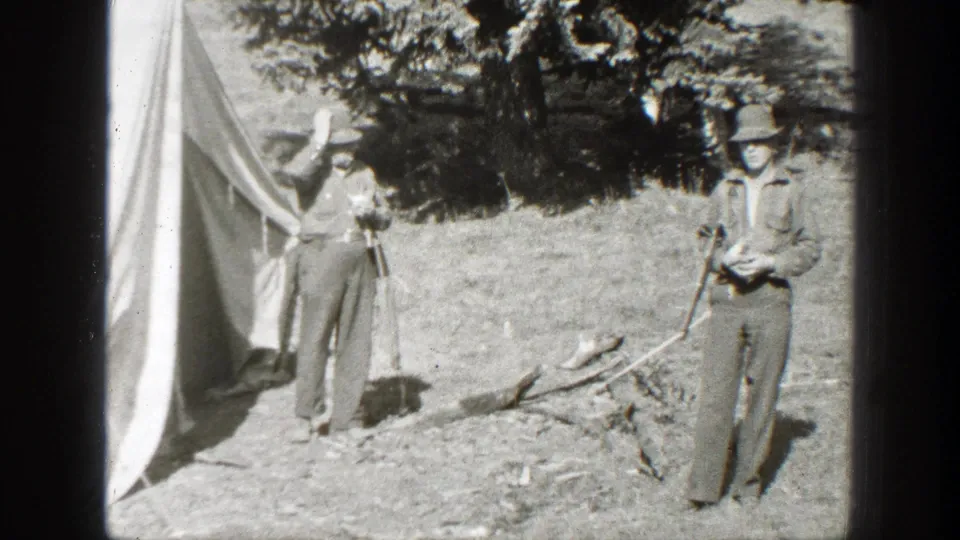 Men in outdoor clothing stand near a canvas tent and branches in 1938 California camp footage.