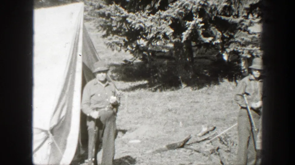 One man stands near the tent opening as another hat-wearing man appears at the edge of the California campsite frame.