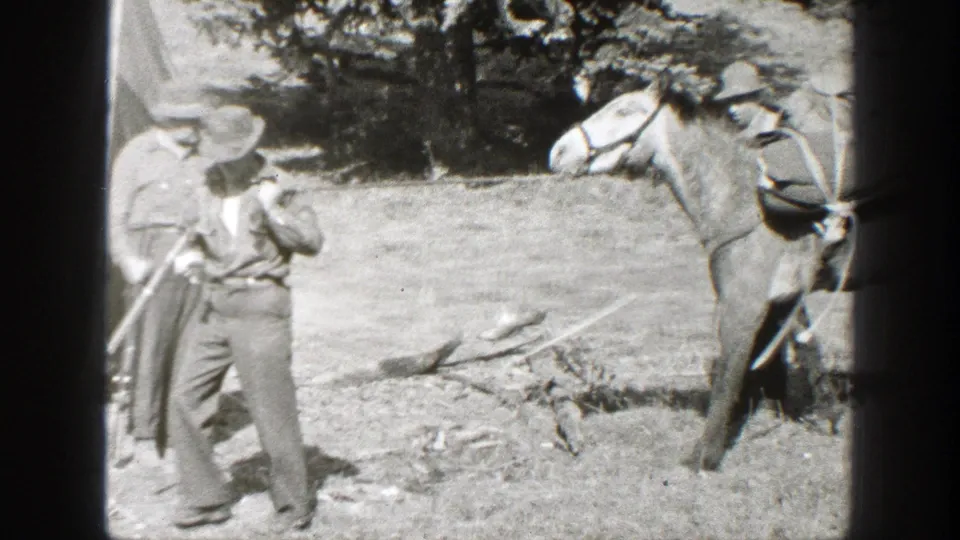 A saddled horse and two adult men appear together in the California camp clearing, suggesting pack or trail travel.