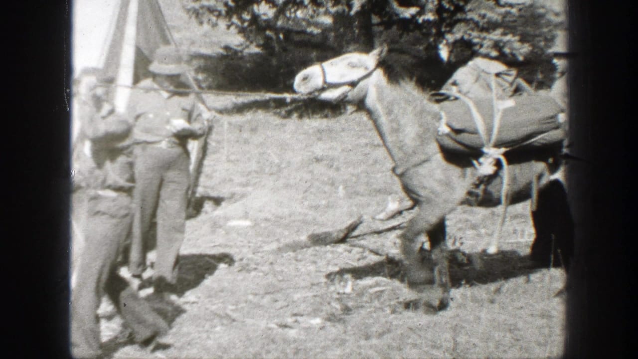 1938 California home-movie frame showing a man with a rifle near a loaded pack mule at a rustic campsite.