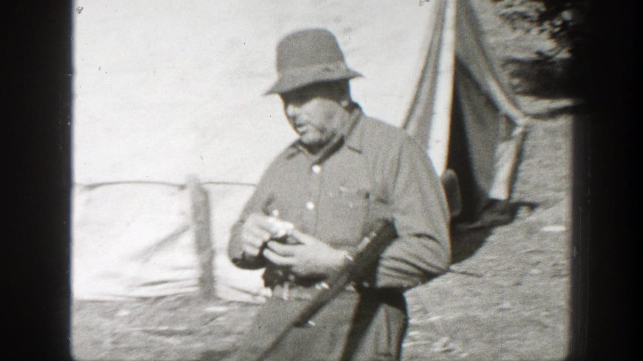 Man in military-style clothing smokes a cigar near a tent while holding a rifle.