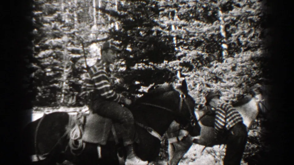 1938 California 8mm frame showing a striped-shirt rider on a saddled horse as another person tends a second horse in the woods.