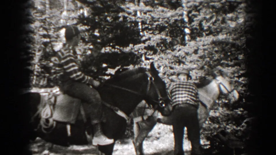 1938 California 8mm frame with a mounted rider and another person working beside a lighter horse among trees.