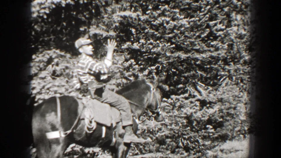 1938 California 8mm frame showing an adult rider in a striped shirt raising a rifle while seated on a horse near dense foliage.