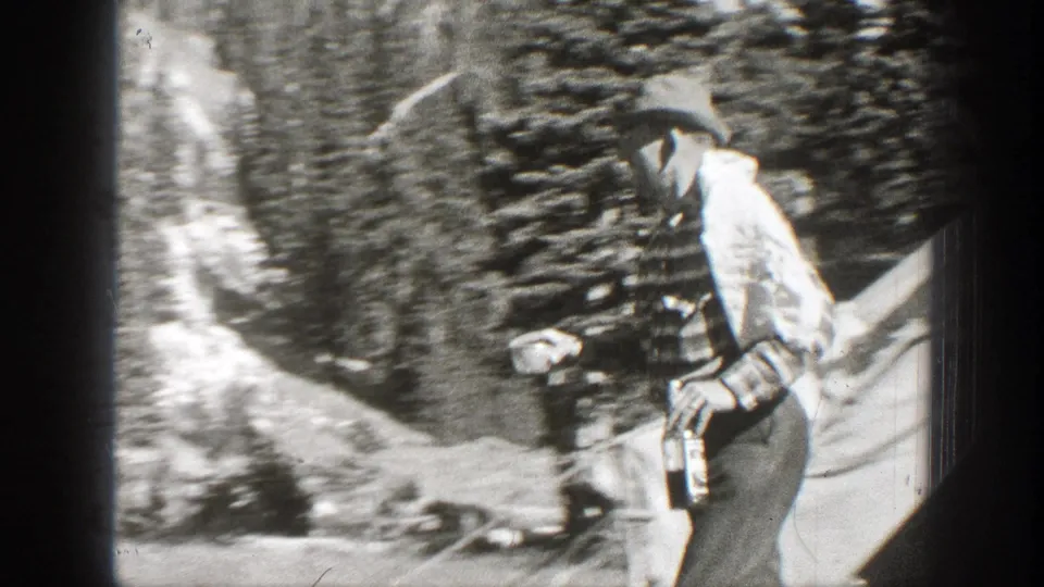 Adult man in a cap and striped shirt carries a bottle while walking through a wooded California slope in 1938 footage.