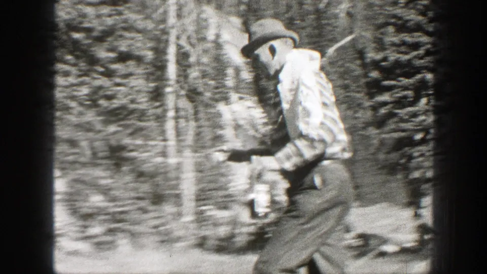 In 1938 California home-movie footage, a man in a brimmed hat walks through a wooded area holding a bottle or container.