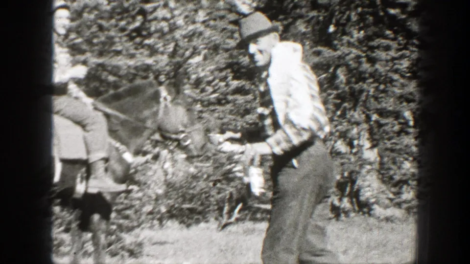 A man in a striped shirt approaches a saddled horse and two nearby figures in wooded California footage from 1938.
