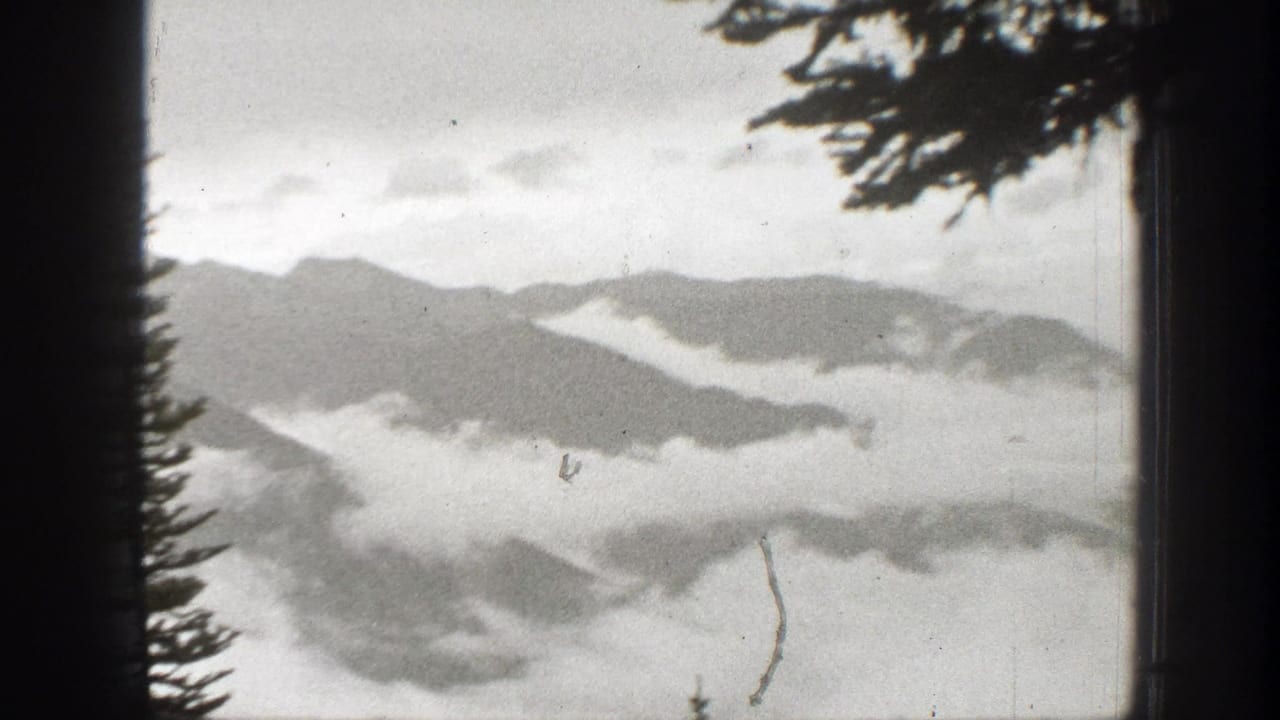 1938 California 8mm frame showing cloud and fog layers across forested mountain ravines with silhouetted conifer edges.