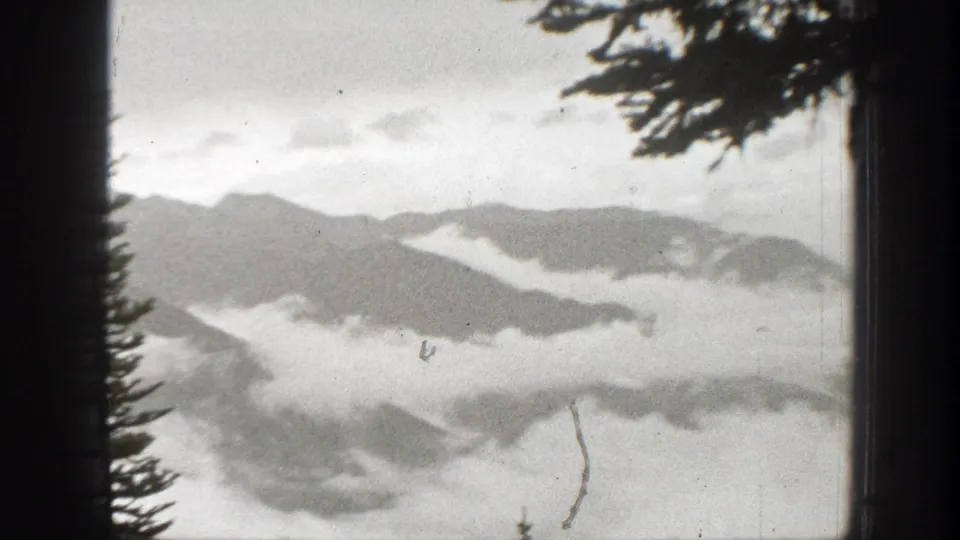 1938 California 8mm frame showing cloud and fog layers across forested mountain ravines with silhouetted conifer edges.