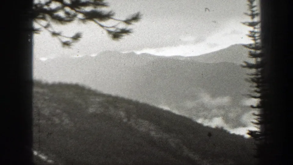 Soft black-and-white 8mm view of California mountain slopes, distant ridgelines, and fog hanging in the valleys.