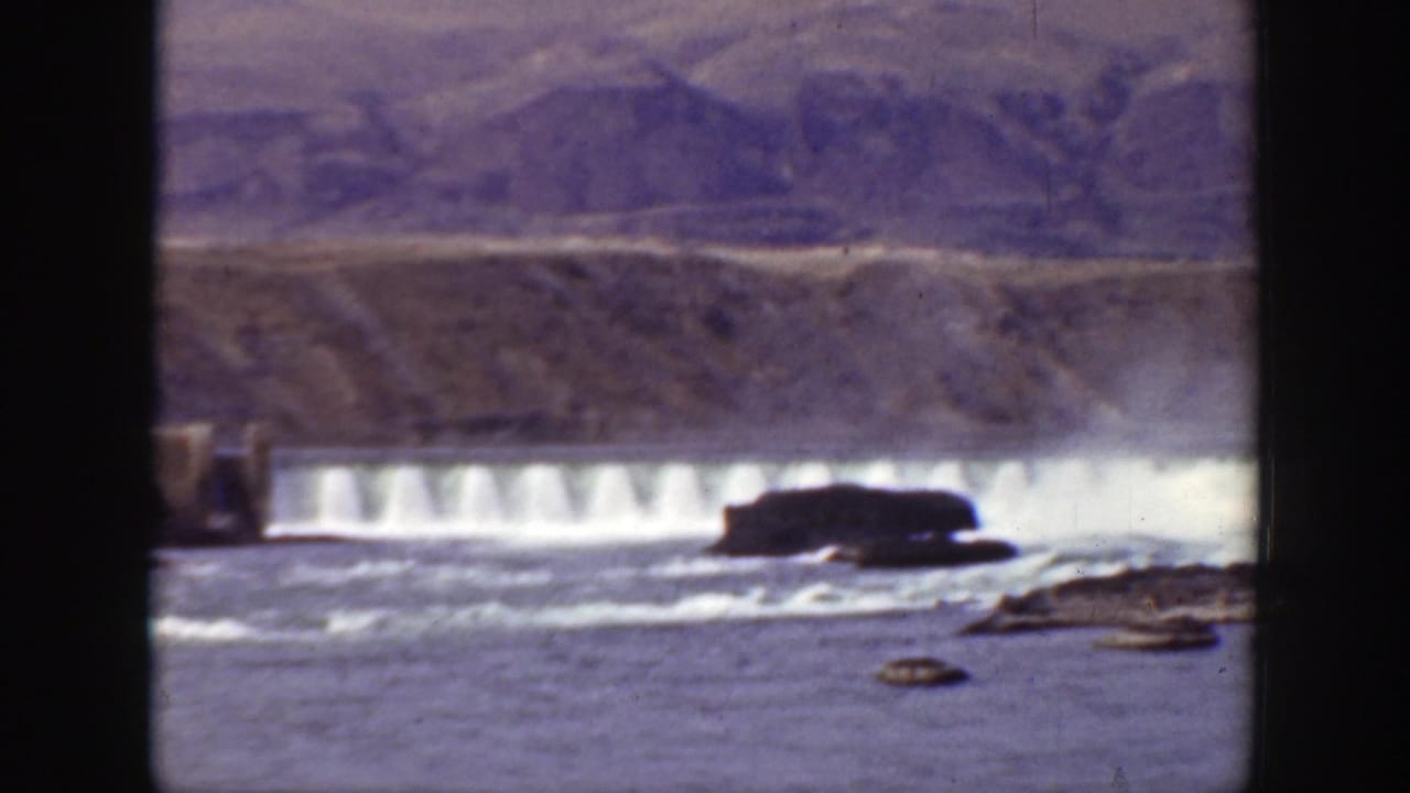 Dam spillway and rocky watercourse seen across a reservoir edge.