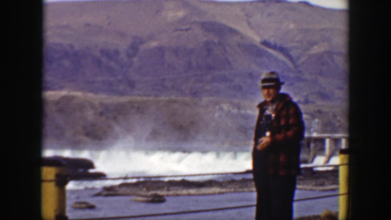 In 1938 California footage, a man in a gray hat stands by a dam spillway with mountains and water spray in the background.