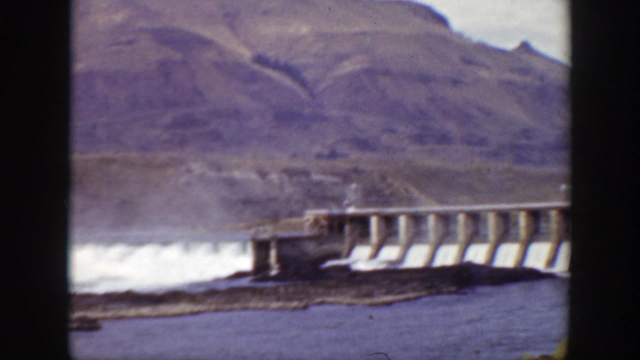 Dam spillway viewed across blue water with white spray near the structure.