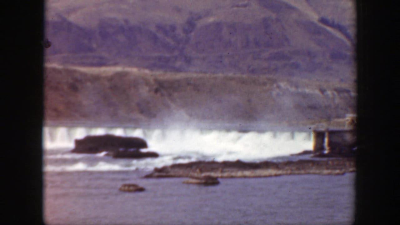 Dam releasing white water below rugged hills with rocks in the foreground.