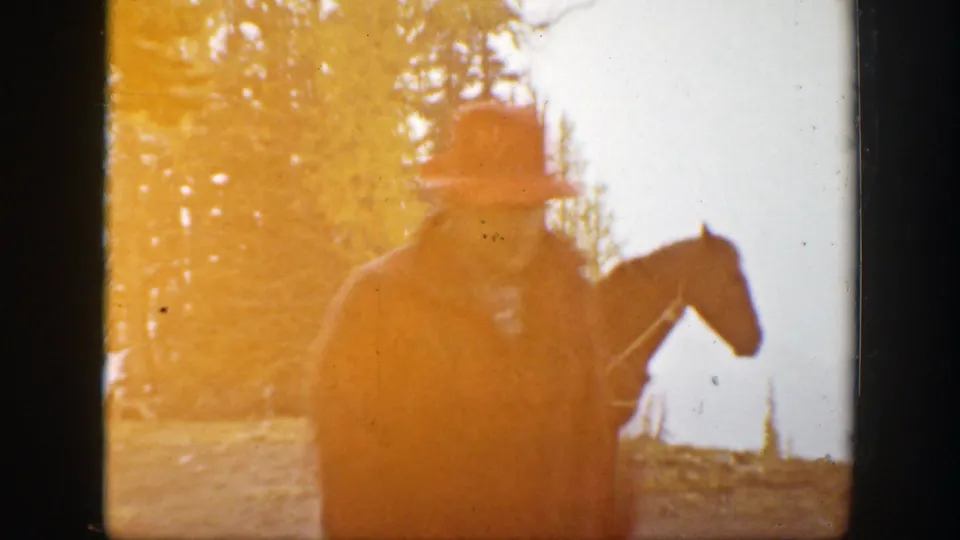 1938 California home-movie frame with a man in outdoor clothing near a horse, partly obscured by warm light flare and trees.