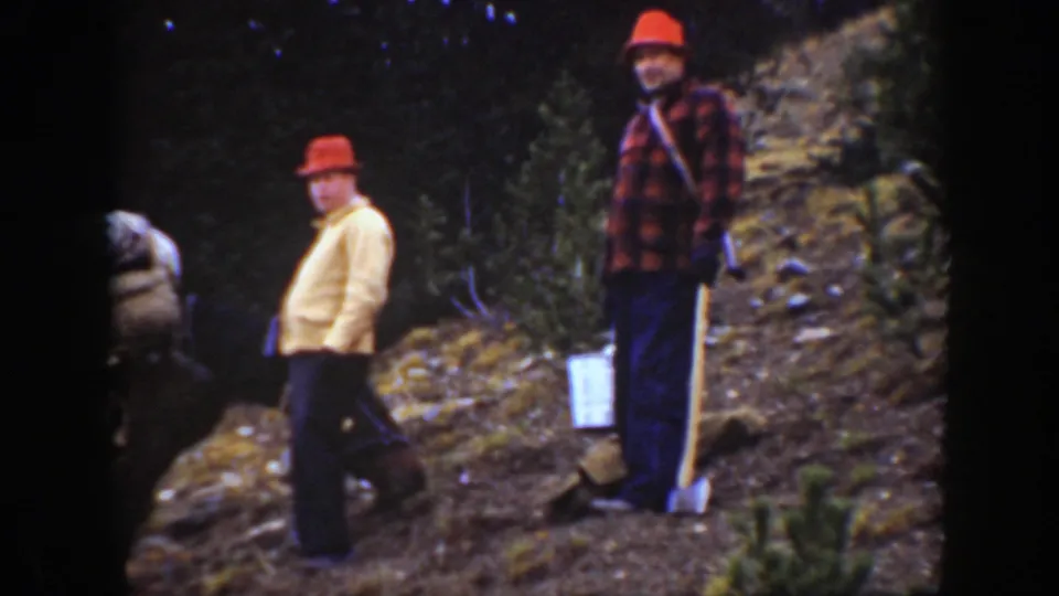 1938 California 8mm frame showing two men in work clothes pausing on a steep forest hillside near a loaded mule.