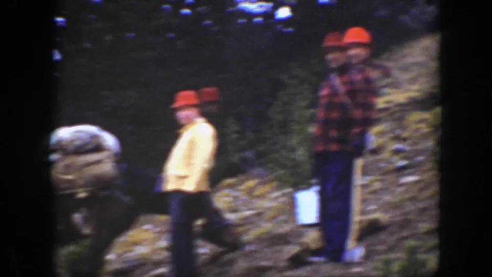 1938 California 8mm frame showing two men on a rocky pine hillside with a loaded mule and trail supplies nearby.