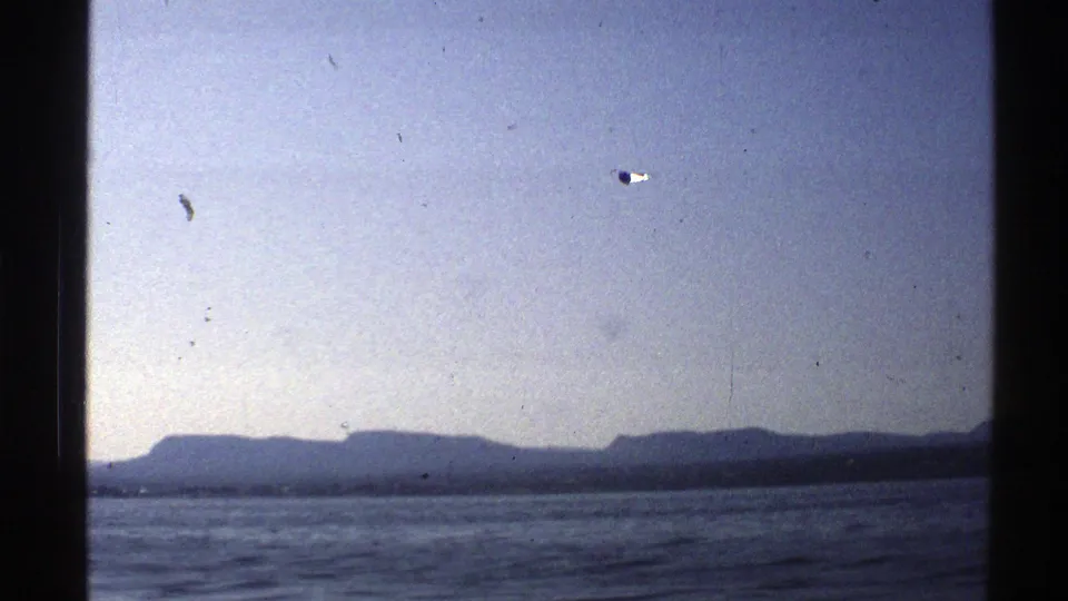 1976 Norway 8mm frame with open water, dark mountain ridges, pale sky, and visible scan texture.