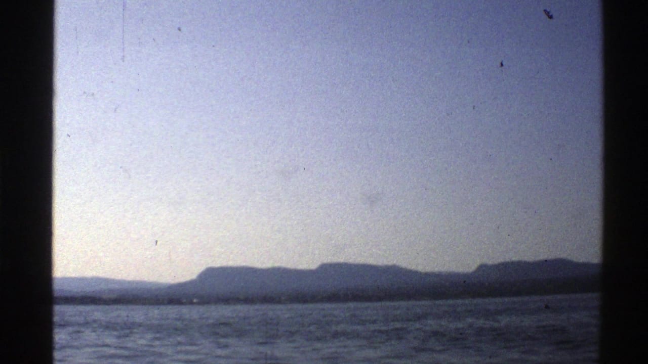 Open water with a distant low mountain horizon under pale sky, framed by dark film edges.