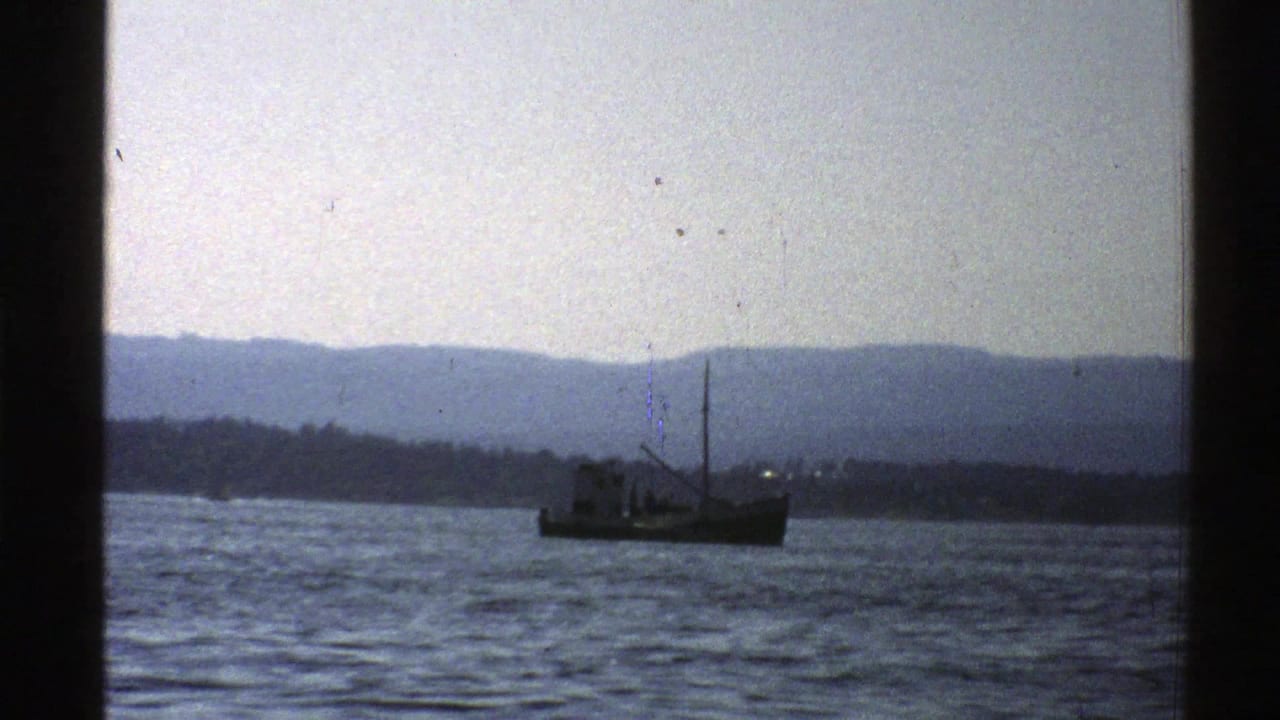 1976 Norway 8mm frame showing a small fishing boat on rippled coastal water with hazy mountains in the distance.