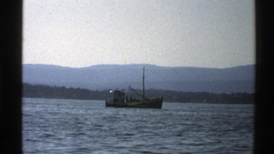 Final 1976 Norway 8mm frame showing the small boat farther across the water with shoreline and mountains behind.