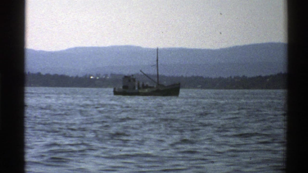 Fishing boat on open water with mountain ridges in the background.
