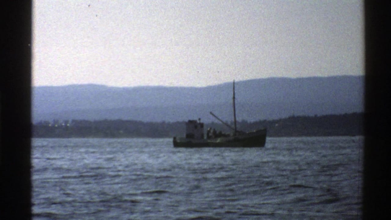 Small boat on calm water with distant shoreline and mountains behind it.