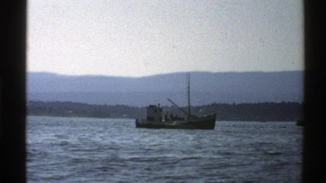 Small boat centered on rippling water with mountains and shoreline in the background.