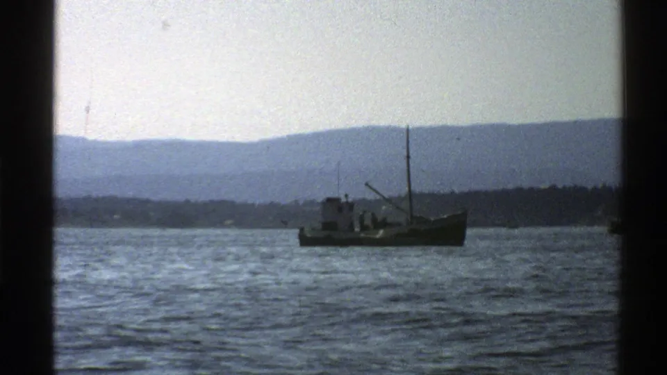 1976 Norway 8mm still with a small boat, distant land, hazy mountains, and visible film-frame edges.