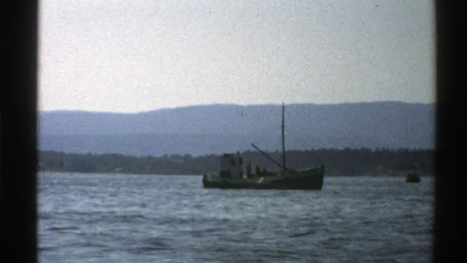 1976 Norway 8mm frame showing the small boat on calm water, with distant mountains and another small craft at right.