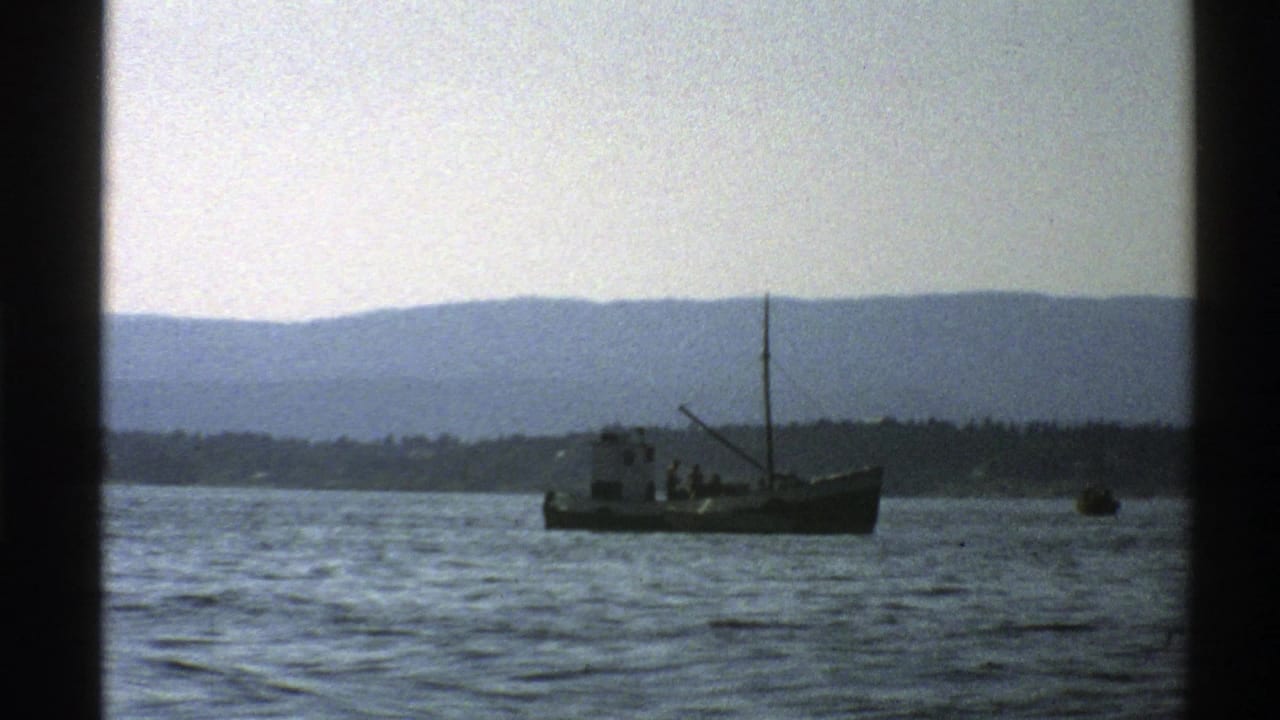 Small boat on rippled water seen through dark window dividers with hills beyond.