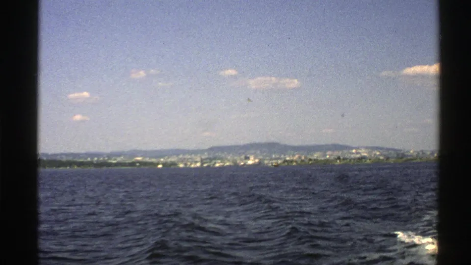 1976 Norway 8mm frame looking over coastal water toward a distant shoreline and hills, with wake visible along the right edge.
