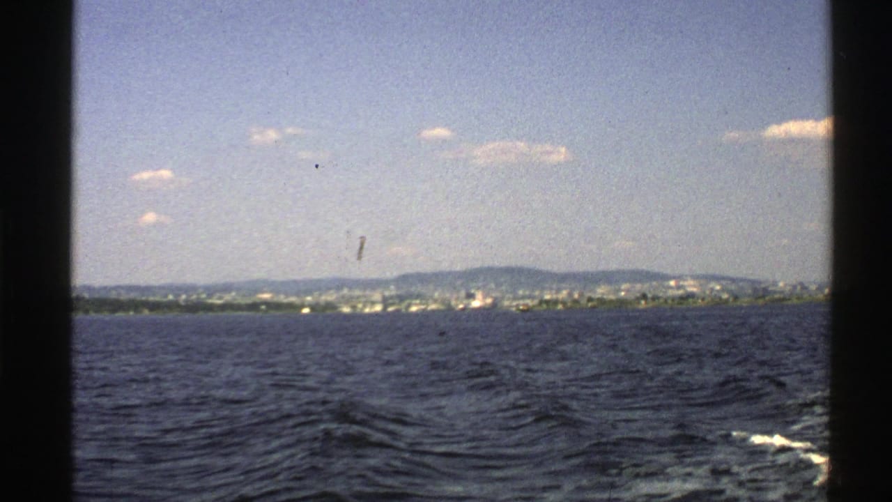 Distant shoreline and hills across open water, seen through dark vertical boat framing.