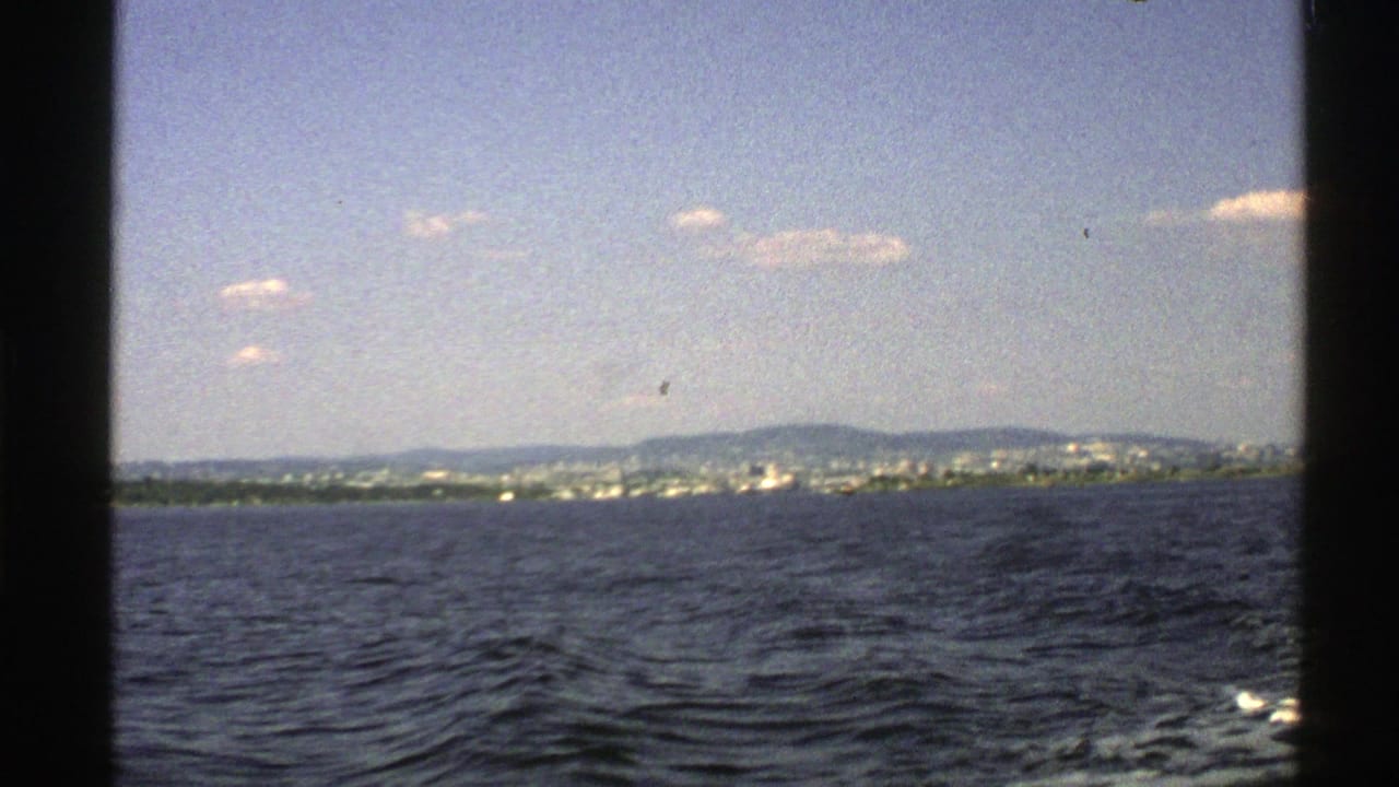 Rippling water seen from a boat with distant hills and shoreline under a pale sky.