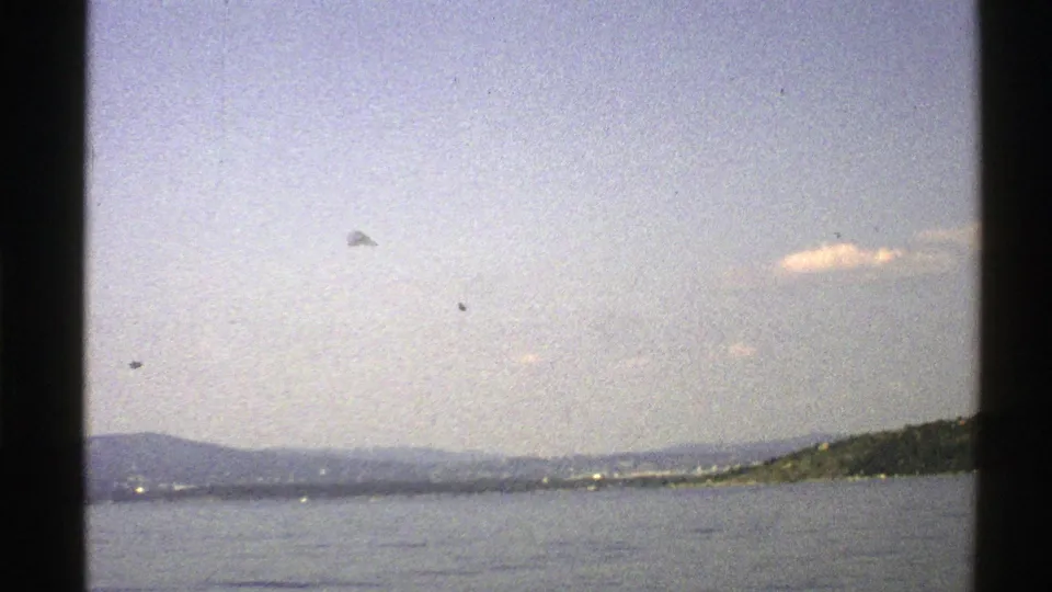 1976 Norwegian 8mm frame of open water, low hills, and a faint shoreline, filmed from a moving boat with visible dust marks.