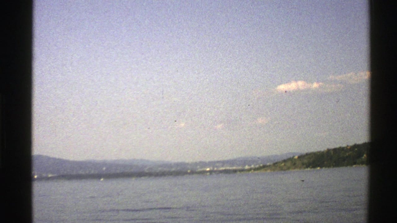 Calm water with distant hills and shoreline seen through dark film-frame edges.