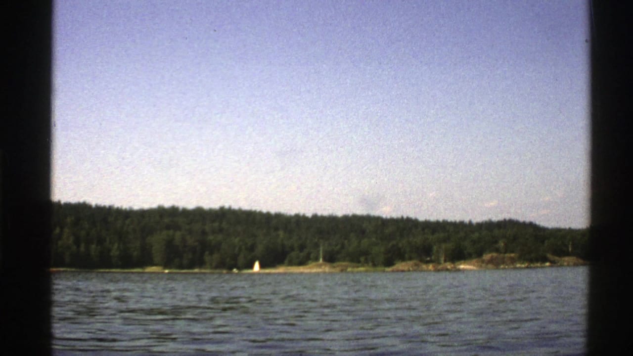 Blue lake water with ripples, forested shoreline, and a small white sailboat in the distance.