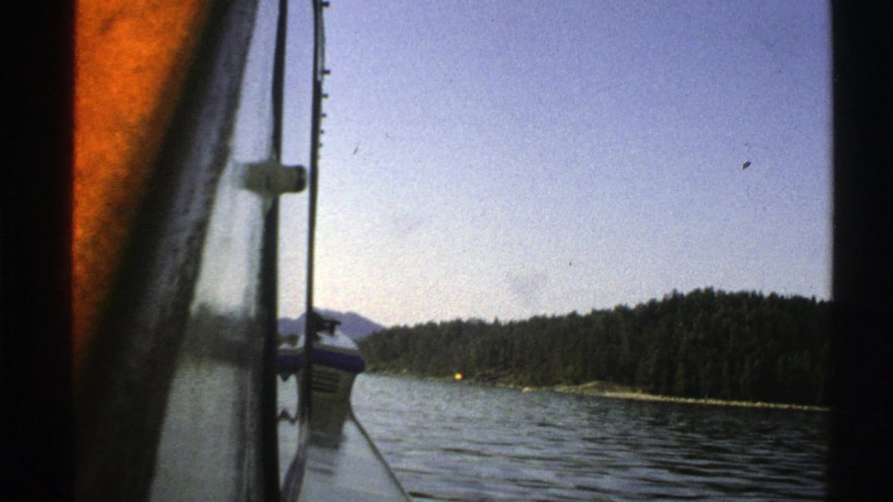 Boat-window view across a lake toward a forested shoreline and distant hills.