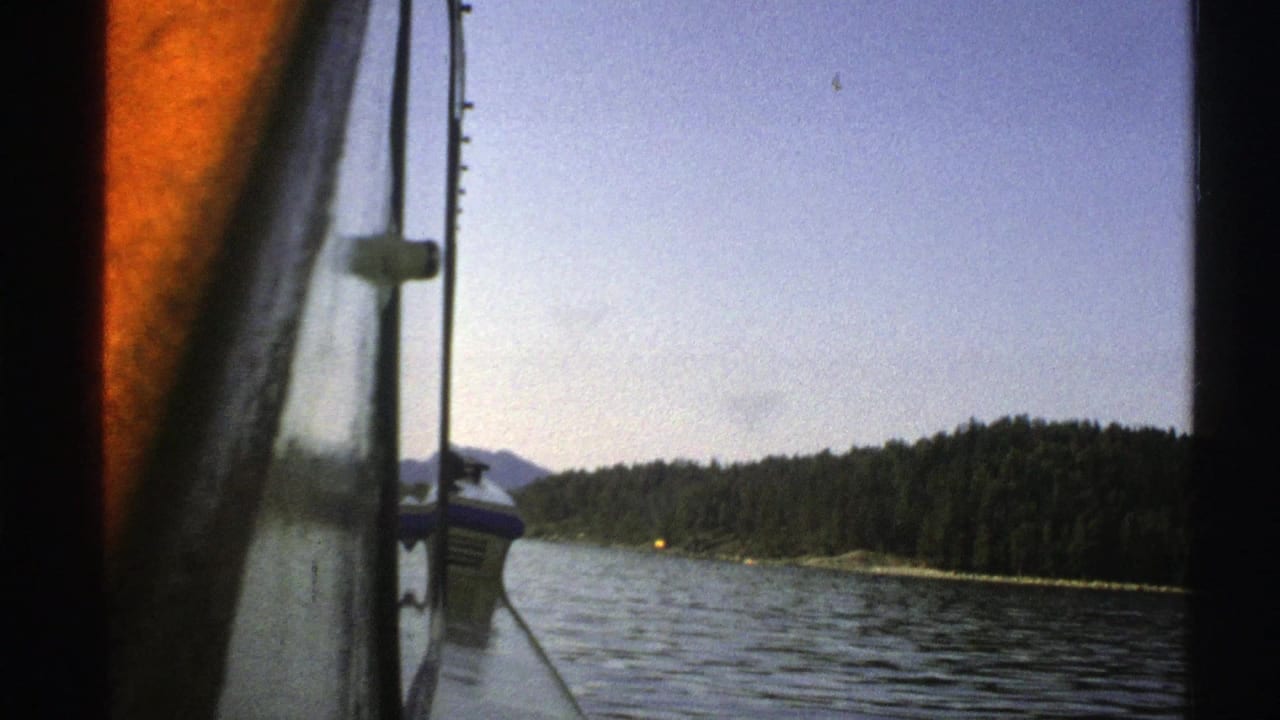 Boat side and window frame in the foreground with lake and wooded shore beyond.