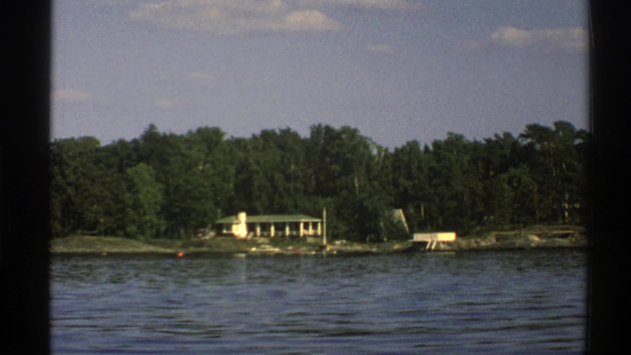 House and dock structures on a forested shore seen over lake water.