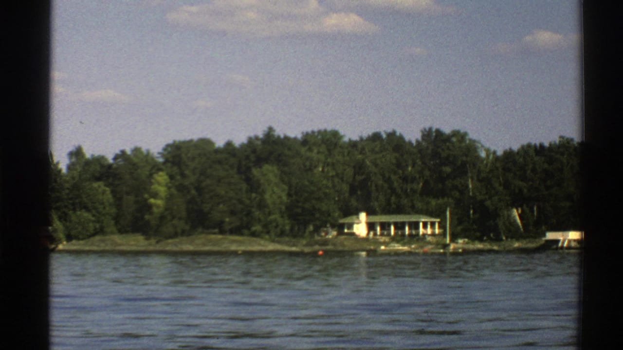 Lake water with small waves, forested shoreline, and a white cottage behind dark 8mm frame borders.