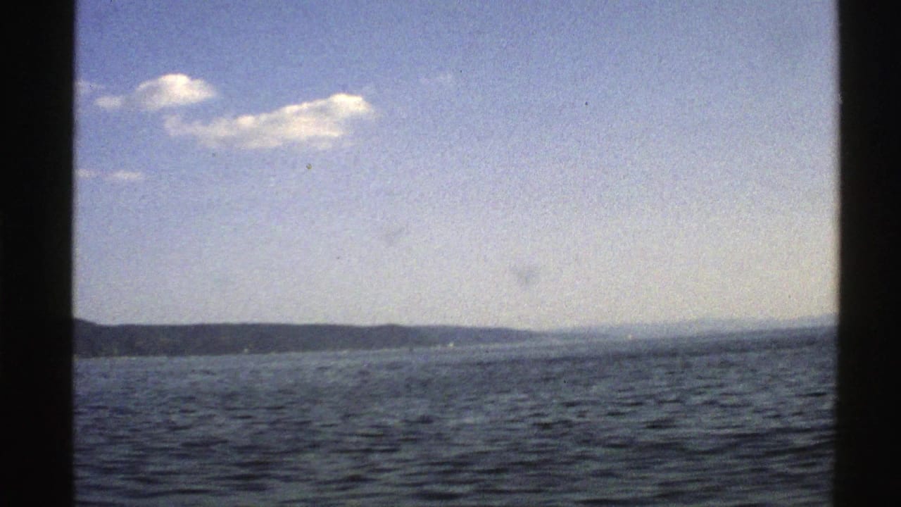 Blue water beneath a pale sky with clouds and a low distant shoreline.