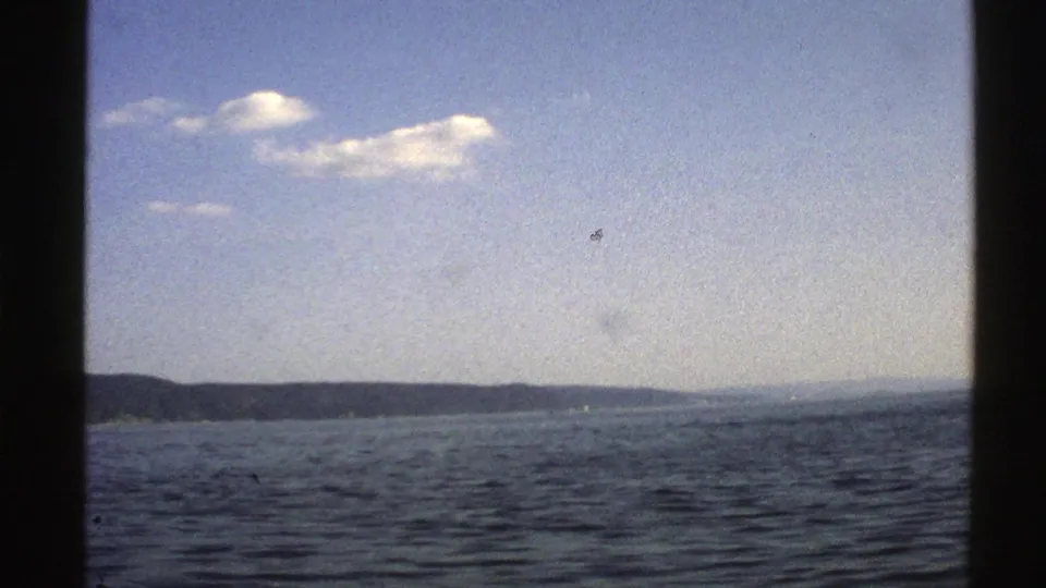 1976 Norway coastal view on 8mm film, with rippling sea, a low peninsula, pale sky, and small clouds framed by dark edges.