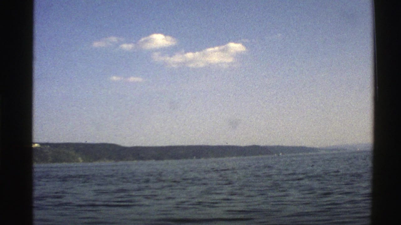 Calm water with a low distant shoreline under blue sky and small clouds.