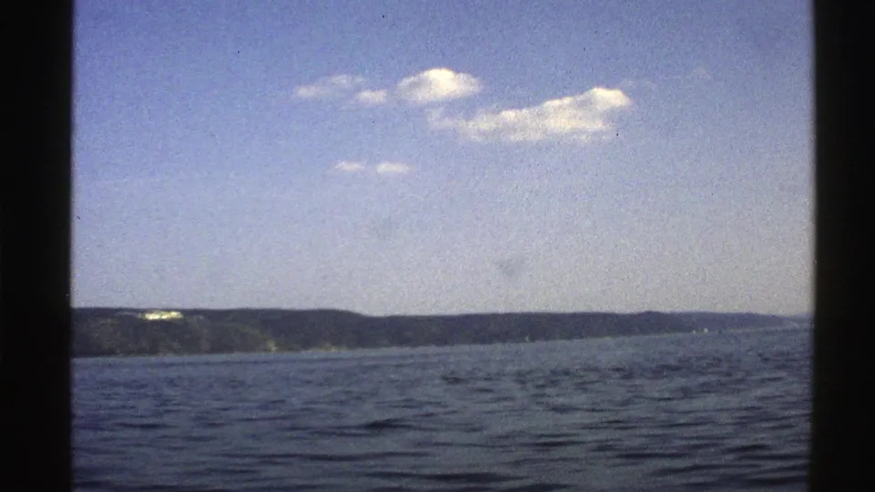1976 Norway 8mm still showing a broad water surface, low green hills, bright sky, and soft home-movie grain.