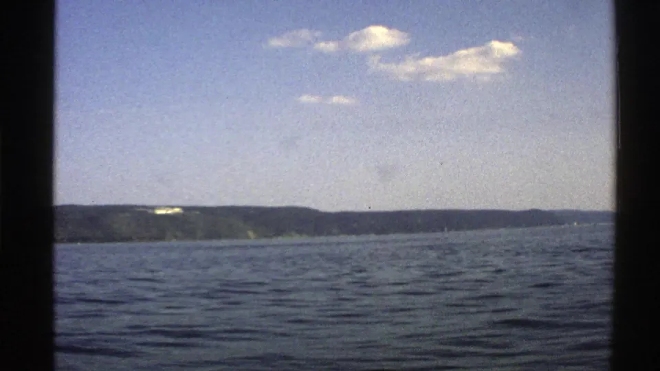 1976 Norway 8mm frame showing open coastal water, a distant low shoreline, pale sky, clouds, and visible film borders.