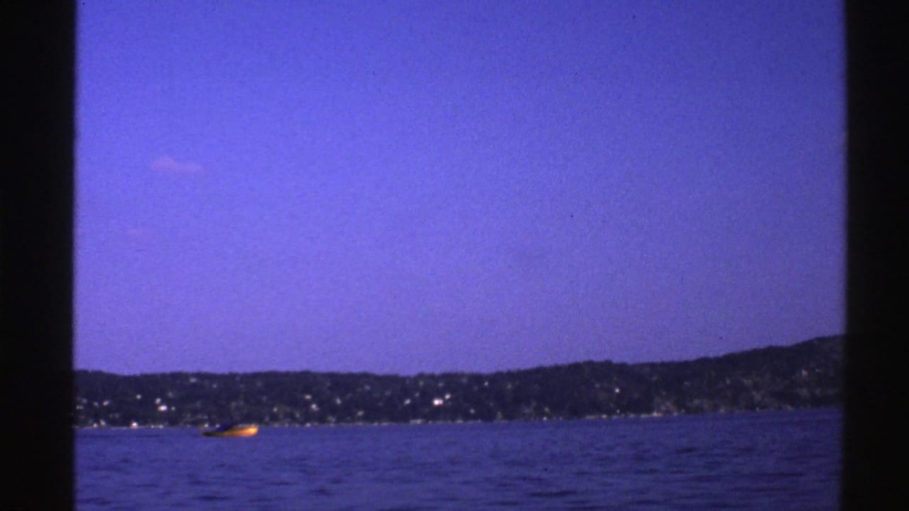 Small yellow boat on blue water with a distant dark shoreline and clear sky.