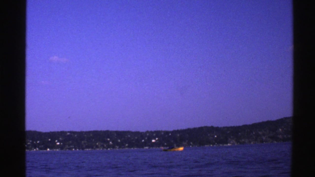 Small yellow boat on dark water near a distant shoreline under a blue sky.