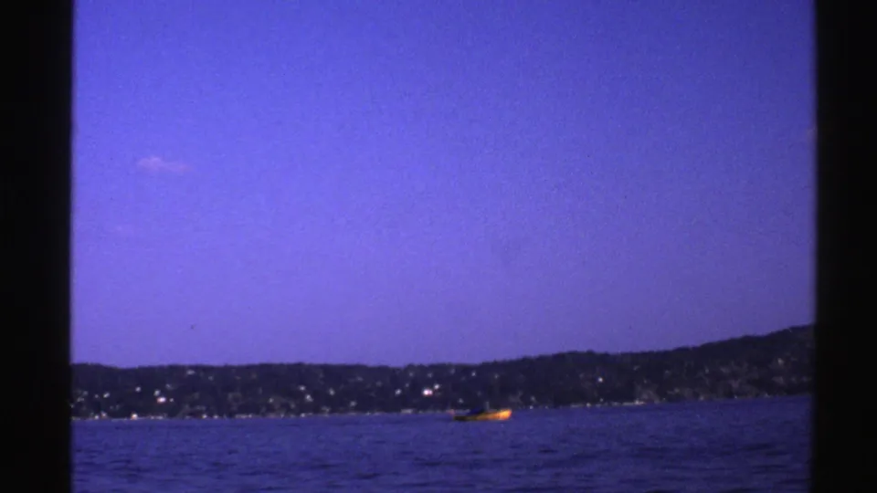 1976 Norway 8mm frame showing a small yellow boat on open water with a distant shoreline and blue sky.